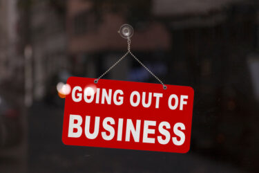 Close-up on a red closed sign in the window of a shop displaying the message "Going out of business".